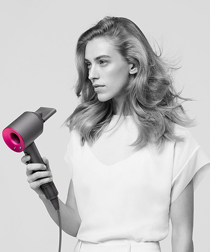 Девушка с феном в руках сушит волосы